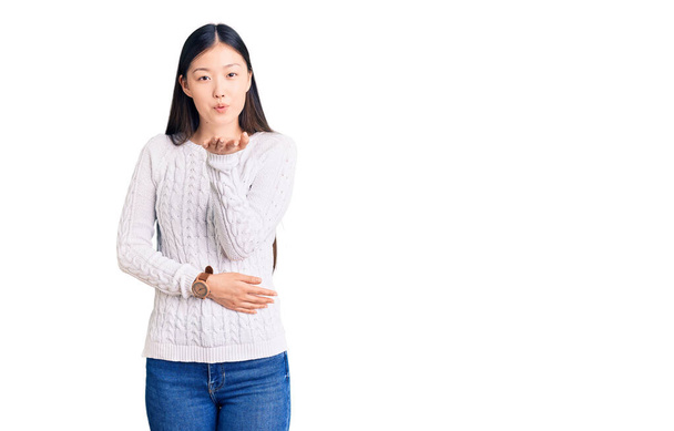 Young beautiful chinese woman wearing casual sweater looking at the camera blowing a kiss with hand on air being lovely and sexy. love expression.  - Foto, Imagem