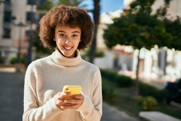Młoda latynoska dziewczyna uśmiechnięta szczęśliwy za pomocą smartfona w mieście. - Zdjęcie, obraz
