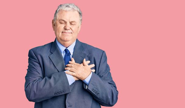 Senior grey-haired man wearing business jacket smiling with hands on chest with closed eyes and grateful gesture on face. health concept.  - Foto, Imagen
