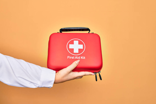 Mano de mujer joven caucásica sosteniendo maletín kit de primeros auxilios sobre fondo blanco aislado - Foto, imagen
