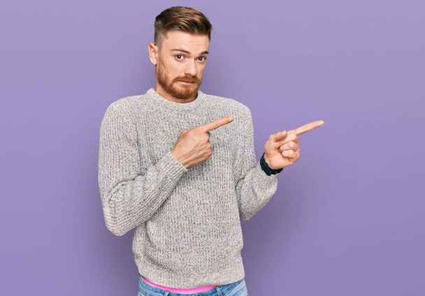Young redhead man wearing casual winter sweater pointing aside worried and nervous with both hands, concerned and surprised expression  - Photo, Image