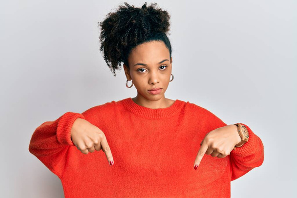 Chica afroamericana joven con ropa casual apuntando hacia abajo mirando triste y molesto, indicando la dirección con los dedos, infeliz y deprimido.  - Foto, imagen