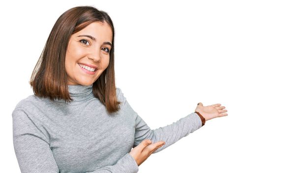 Fiatal gyönyörű nő visel alkalmi garbó pulóver meghívó belépni mosolygós természetes nyitott kézzel  - Fotó, kép