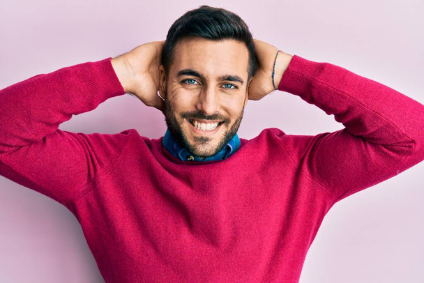 Jeune homme hispanique portant des vêtements décontractés relaxant et étirant, les bras et les mains derrière la tête et le cou souriant heureux  - Photo, image