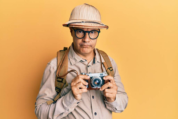 Middle age bald man wearing explorer hat and vintage camera skeptic and nervous, frowning upset because of problem. negative person.  - Foto, Imagem