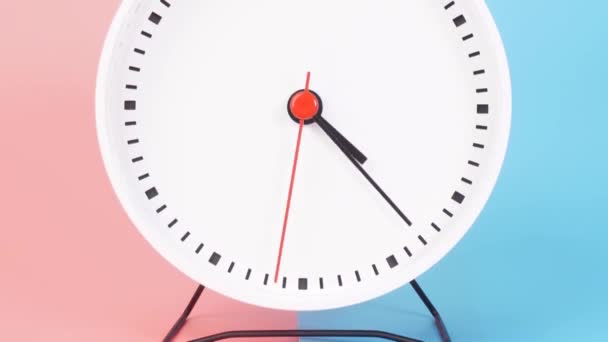 The white clock rotates at a speed for 1 hour from 4:00 AM - 5:00 AM or 4:00 PM - 5:00 PM with a red second hand. The minute and hour hands are black. There are two color backgrounds, blue and pink. - Felvétel, videó