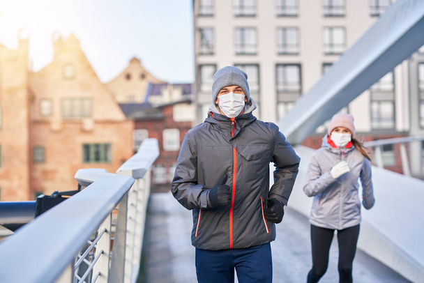 Volwassen paar joggen in de stad in maskers tijdens lockdown - Foto, afbeelding
