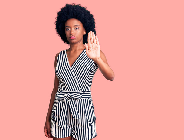 Jonge Afro-Amerikaanse vrouw in casual kleding doet stoppen met zingen met handpalm van de hand. waarschuwingsuitdrukking met negatief en ernstig gebaar op het gezicht.  - Foto, afbeelding
