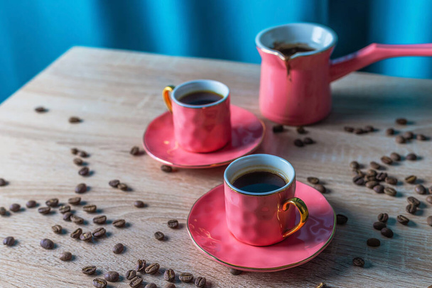 Keramické růžové šálky černé kávy a turka na tyrkysovém pozadí. Moderní světlé barevné pastelové barvy atmosféra - Fotografie, Obrázek