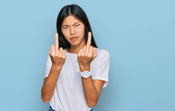 красивая молодая азиатская женщина в повседневной белой футболке показывая средний палец делает трахнуть вас плохое выражение лица, провокация и грубое отношение. Крики возбужденных  - Фото, изображение
