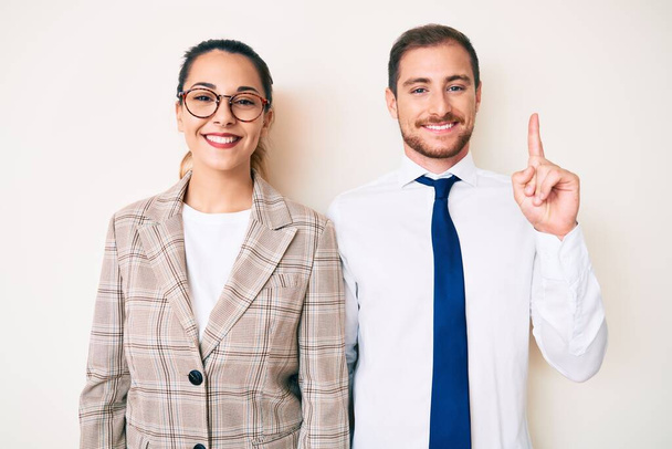 Beautiful couple wearing business clothes showing and pointing up with finger number one while smiling confident and happy.  - Фото, изображение