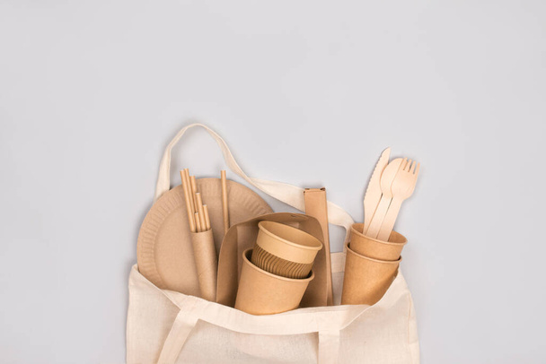 Eco-friendly tableware - kraft paper food cups and containers in cotton bag on gray background with copy space. Street food take away paper packaging - cups, plates, straws. Selective focus - Photo, Image