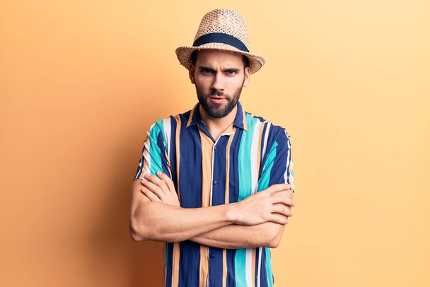 Young handsome man with beard wearing summer hat and shirt skeptic and nervous, disapproving expression on face with crossed arms. negative person.  - Photo, Image