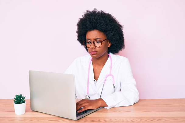 Mladý africký americký žena na sobě lékař stetoskop pracuje pomocí počítače notebook myšlení postoj a střízlivý výraz hledá sebevědomí  - Fotografie, Obrázek