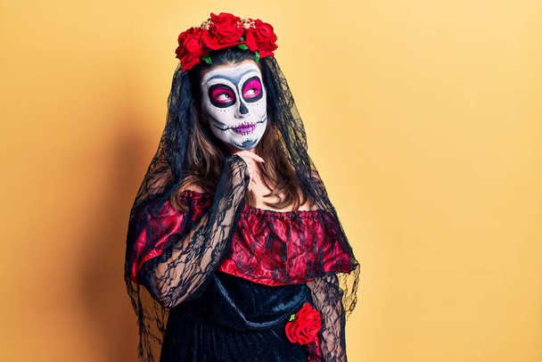 Young woman wearing day of the dead costume over yellow with hand on chin thinking about question, pensive expression. smiling with thoughtful face. doubt concept.  - Photo, image
