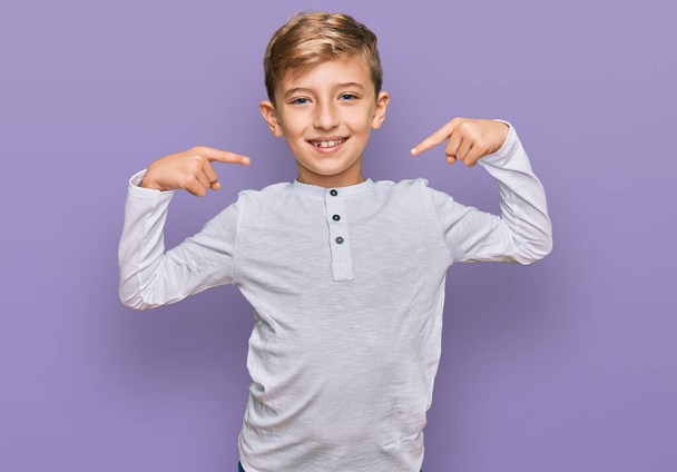 Malý kavkazský chlapec, oblečený do neformálního oblečení, vesele se usmívající a ukazující prstem na zuby a ústa. koncepce stomatologického zdraví.  - Fotografie, Obrázek