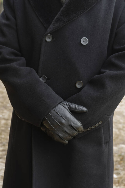 Κοντινό πλάνο του σωματικού τμήματος του αρσενικού, που στέκεται έξω. Σώμα αγνώριστου άνδρα με μαύρο παλτό και μαύρα δερμάτινα γάντια. - Φωτογραφία, εικόνα