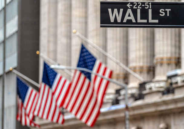 Wall Street "WALL ST" sign and broadway street over American national flags in front of NYSE stock market exchange building background. The New York Stock Exchange locate in economy district - Photo, Image