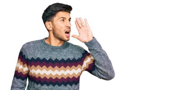 Young handsome man wearing casual winter sweater shouting and screaming loud to side with hand on mouth. communication concept.  - Photo, Image
