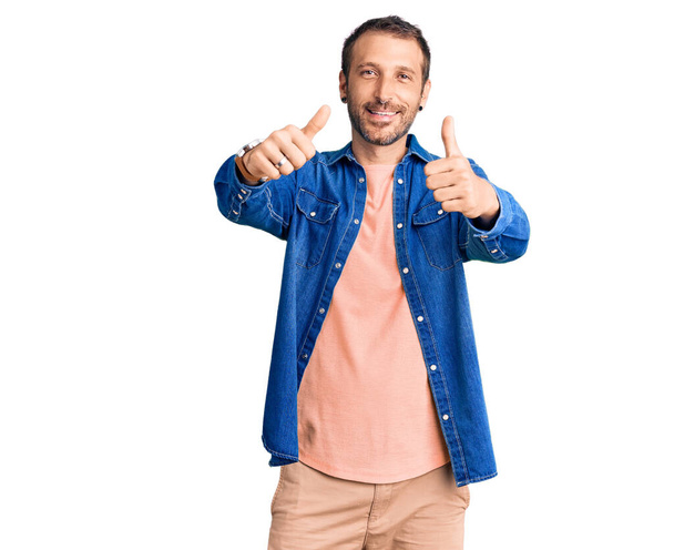Young handsome man wearing casual clothes approving doing positive gesture with hand, thumbs up smiling and happy for success. winner gesture.  - Photo, Image