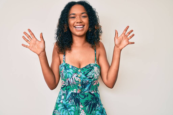 Junge afrikanisch-amerikanische Frau trägt lässige Kleidung und zeigt mit den Fingern Nummer zehn nach oben, während sie selbstbewusst und glücklich lächelt.  - Foto, Bild