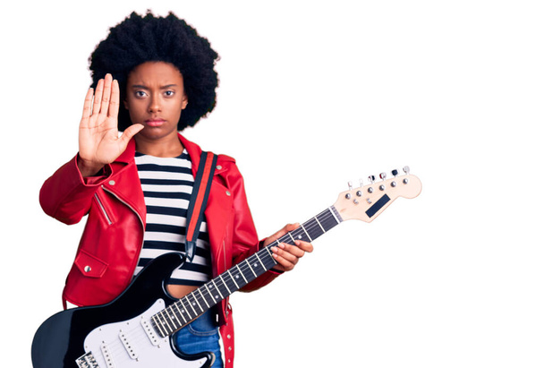 Молода афроамериканська жінка, що грає на електричній гітарі з відкритою рукою робить стоп знак з серйозним і впевненим виразом, захисний жест  - Фото, зображення