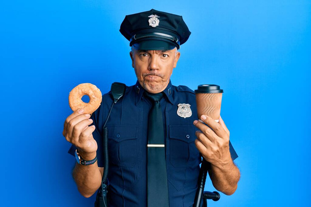 Yakışıklı, olgun, donut yiyen, kahvesini yudumlayan şüpheci ve gergin bir orta yaşlı polis sorun yüzünden surat asıyor. negatif kişi.  - Fotoğraf, Görsel