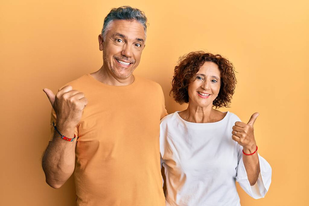 Schönes Paar mittleren Alters in lässiger Kleidung, die nach hinten zeigt, mit Hand und Daumen nach oben, selbstbewusst lächelnd  - Foto, Bild