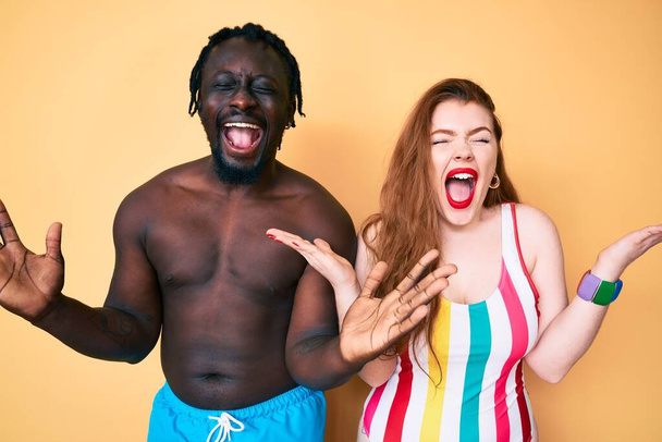 Couple Interracial portant des maillots de bain célébrant fou et fou de succès avec les bras levés et les yeux fermés hurlant excités. concept gagnant  - Photo, image