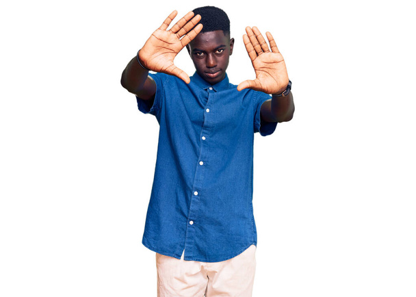 Молодой африканский американец в повседневной одежде делает рамку с помощью ладоней и пальцев, камеры перспективы  - Фото, изображение