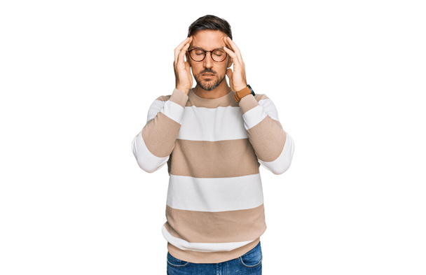 Knappe man met baard in casual kleding en bril met de hand op het hoofd, hoofdpijn omdat stress. lijden aan migraine.  - Foto, afbeelding