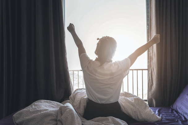 Вид сзади женщины, растягивающейся и лежащей в постели после пробуждения, вступающей в новый день со счастьем и расслабленными выходными - Фото, изображение