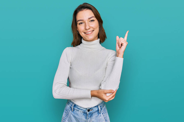 Young caucasian girl wearing casual clothes with a big smile on face, pointing with hand and finger to the side looking at the camera.  - Photo, Image