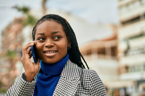 Genç afro-amerikan iş kadını gülümseyerek şehirdeki akıllı telefondan konuşuyor.. - Fotoğraf, Görsel