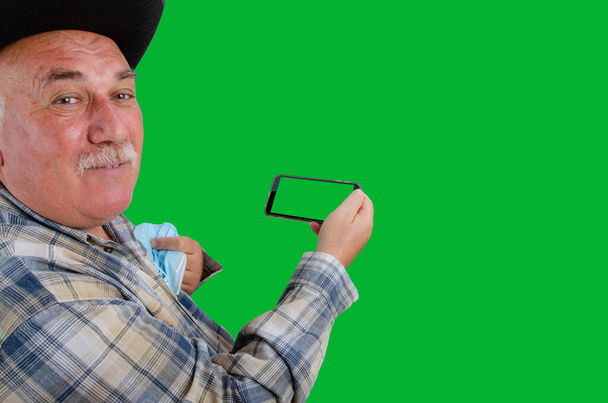 Un vieux villageois en chemise à carreaux sourit en regardant la caméra. Il tient un téléphone portable avec un écran vert dans la main. On dirait qu'il a eu de bonnes nouvelles par application de télémédecine. - Photo, image