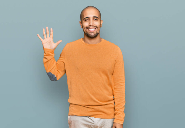 Hispánec dospělý muž na sobě ležérní zimní svetr ukazující a ukazující s prsty číslo pět a zároveň se usmívá sebevědomě a šťastně.  - Fotografie, Obrázek