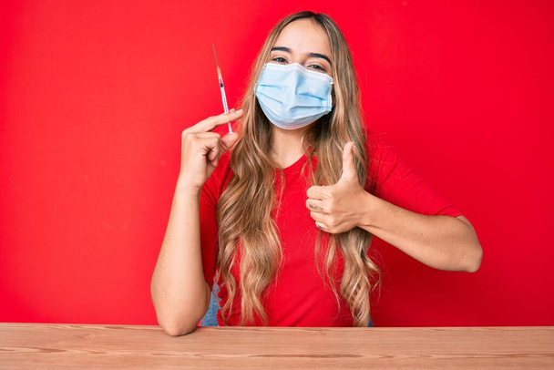 Young beautiful blonde woman holding syringe smiling happy and positive, thumb up doing excellent and approval sign  - Foto, Bild
