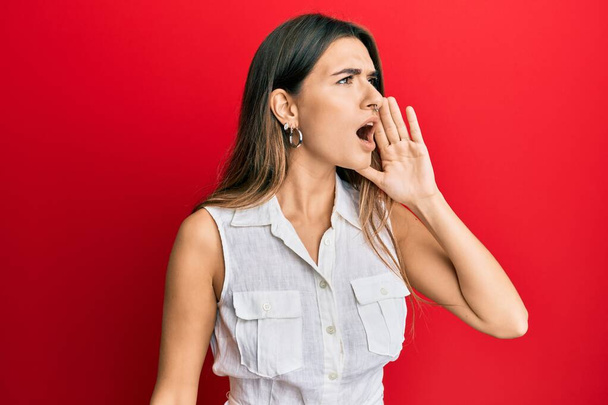 Young hispanic woman wearing casual clothes shouting and screaming loud to side with hand on mouth. communication concept.  - Фото, изображение