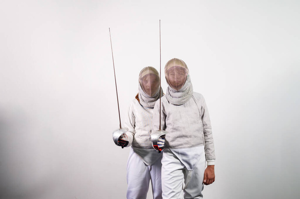 Teenage girls in fencing costumes with swords in their hands isolated on white studio background. Young people practice and practice fencing. Sports, healthy lifestyle. - Photo, image