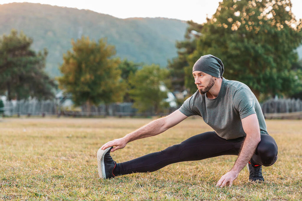 Sport et yoga. Un homme avec une barbe, en tenue de sport effectue des étirements sur l'herbe avant l'entraînement. Espace de copie. - Photo, image