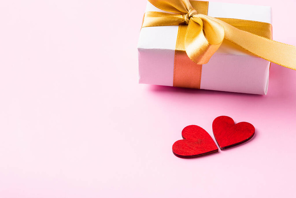 Valentin napi háttérkoncepció. Fehér ajándék doboz egy arany íj szalag és fa piros szív összetétele üdvözlő kártya boldog szerelem elszigetelt rózsaszín háttér másolási hely. Kilátás felülről - Fotó, kép