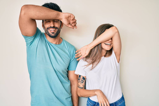 Beautiful young couple of boyfriend and girlfriend together covering eyes with arm smiling cheerful and funny. blind concept.  - Foto, Imagen