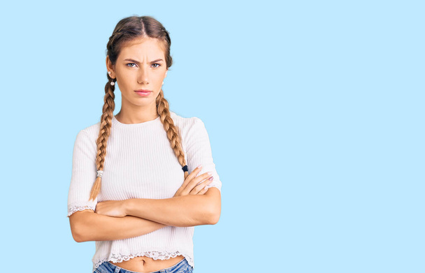 Beautiful caucasian woman with blonde hair wearing braids and white tshirt skeptic and nervous, disapproving expression on face with crossed arms. negative person.  - Photo, Image