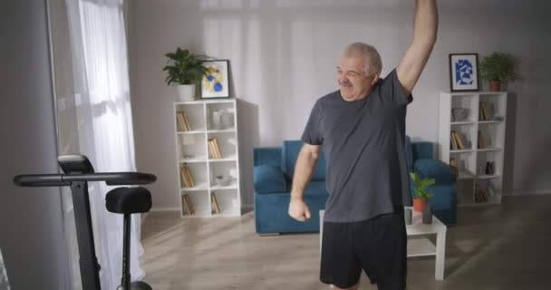 mężczyzna w średnim wieku z bólem kręgosłupa robi gimnastykę w domu, leczenie i zapobieganie chorobom kręgosłupa - Materiał filmowy, wideo
