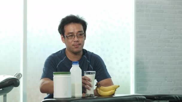 Jeune homme asiatique en vêtements de sport assis et boire du lait après la formation de poids dans le gymnase. sport, musculation, fitness et concept de personnes - Séquence, vidéo