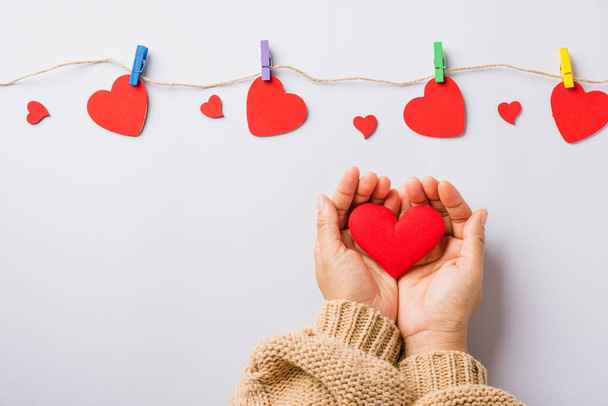 Valentine's day and birthday. Woman hands holding red heart present decorated surprise on white background, Female's hand hold gift heart on hands, Top view flat lay composition - 写真・画像