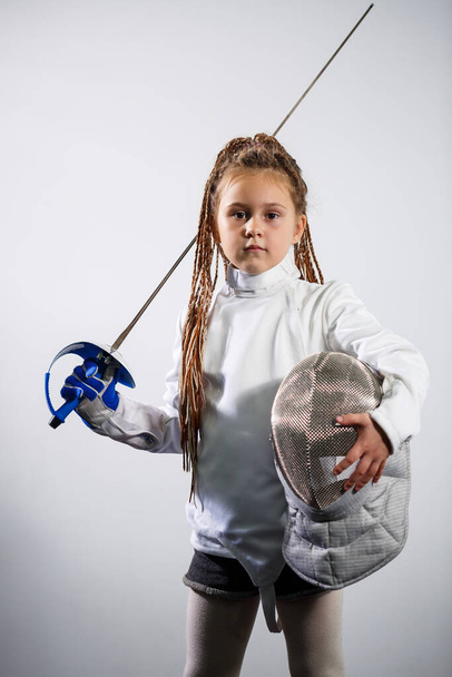 A child in a fencing costume is holding an epee. Girl learning fencing - Photo, image
