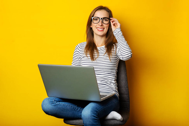 Junge Frau auf Stuhl arbeitet am Laptop auf gelbem Hintergrund. - Foto, Bild