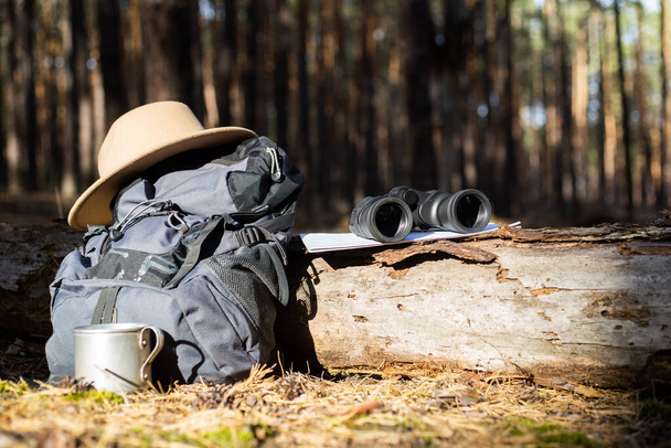Toeristische rugzak, hoed, verrekijker en een kaart op een boomstam in het bos. Concept wandelen, wandelen in de bergen. - Foto, afbeelding