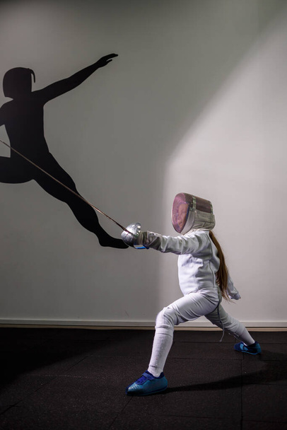 剣を手にしたフェンシングのスーツの少女。若い女性モデル練習と運動。スポーツ、健康的なライフスタイル. - 写真・画像